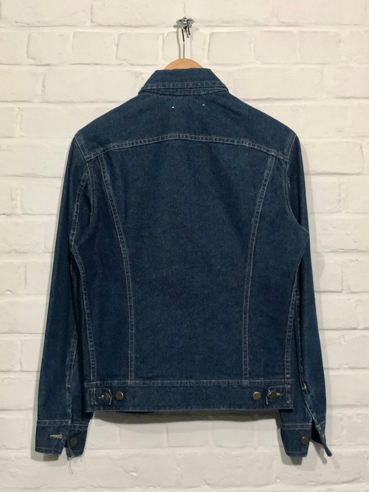 Blue denim jacket on a hanger against a white brick wall