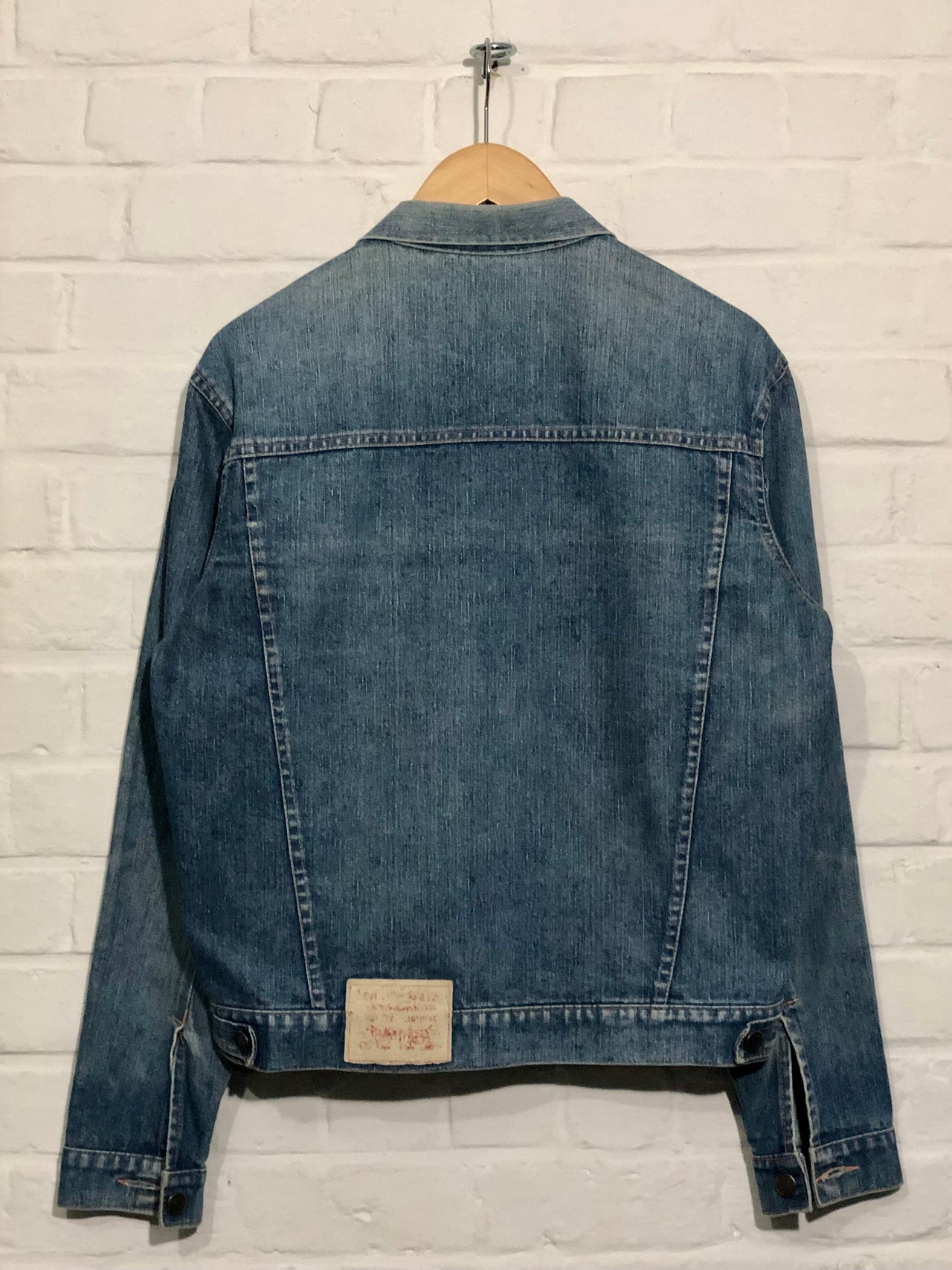 Blue denim jacket on a hanger against a light brick wall.
