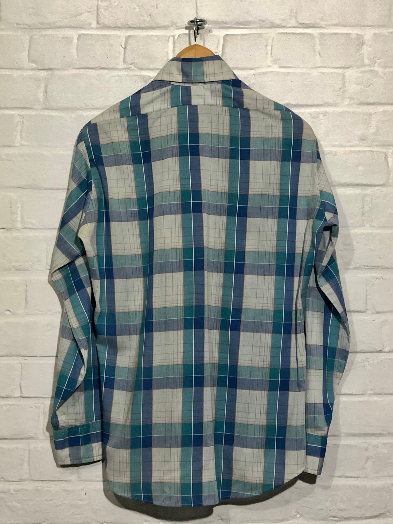 Plaid shirt on a hanger against a white brick wall