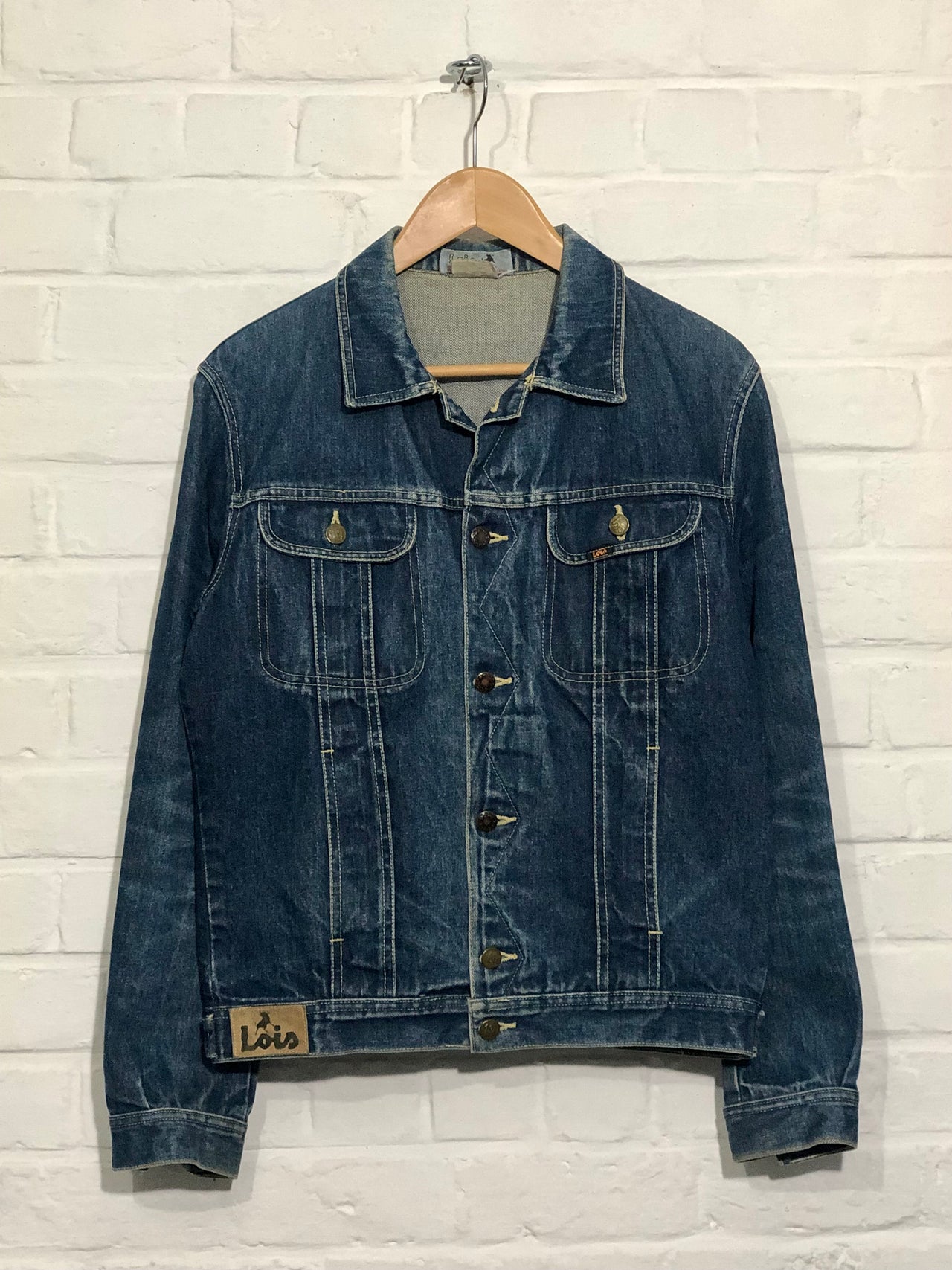 Blue denim jacket on a hanger against a white brick wall