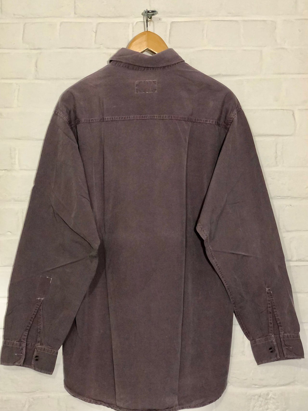 Dark brown shirt on a hanger against a light brick wall.