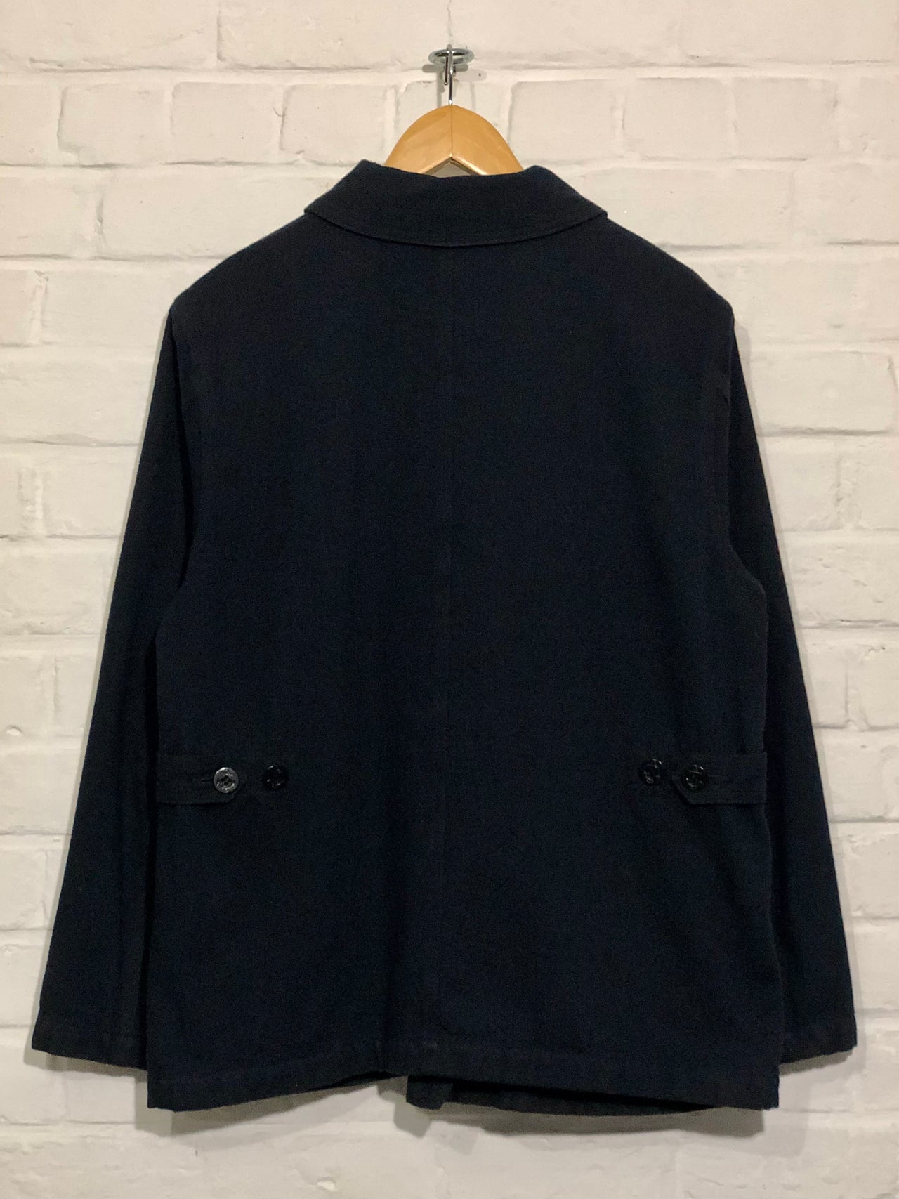 Black coat with gold accents on a hanger against a white brick wall.